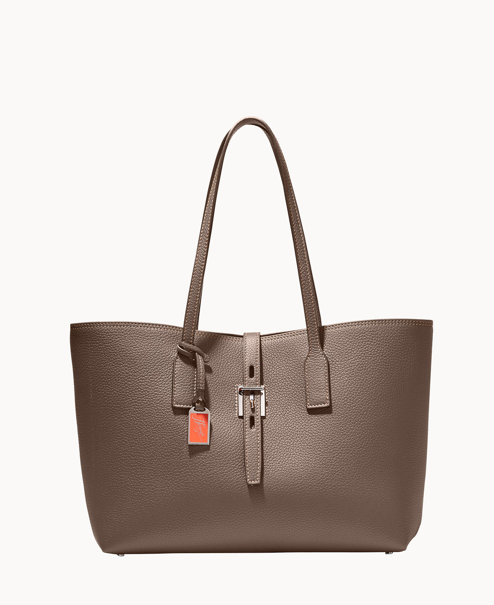 A taupe leather tote bag with double handles, a front belt detail with a silver buckle, and an orange rectangular tag hanging from one handle, set against a plain white background.