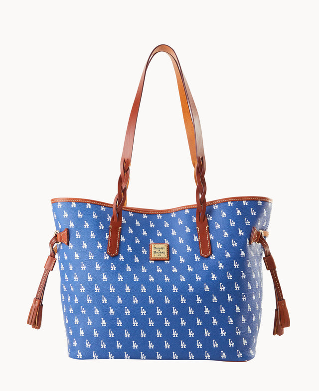 A blue tote bag with brown leather handles and tassels, featuring a repeating white LA logo pattern and a small gold Dooney & Bourke label on the front.