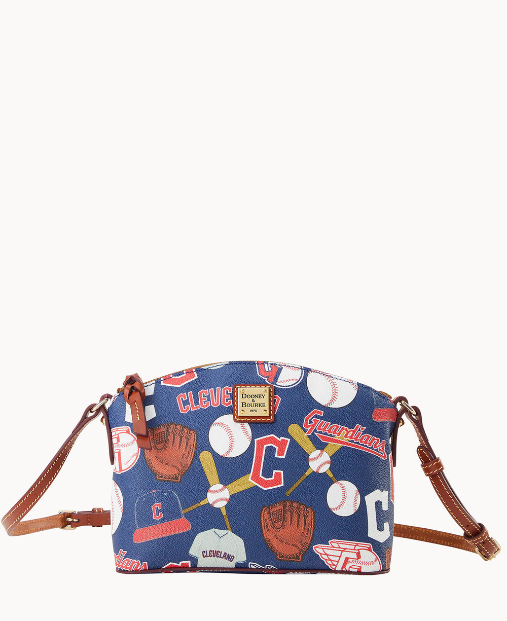A blue crossbody bag with brown leather straps, featuring a baseball-themed print with gloves, bats, balls, and the words Cleveland Guardians along with team logos.