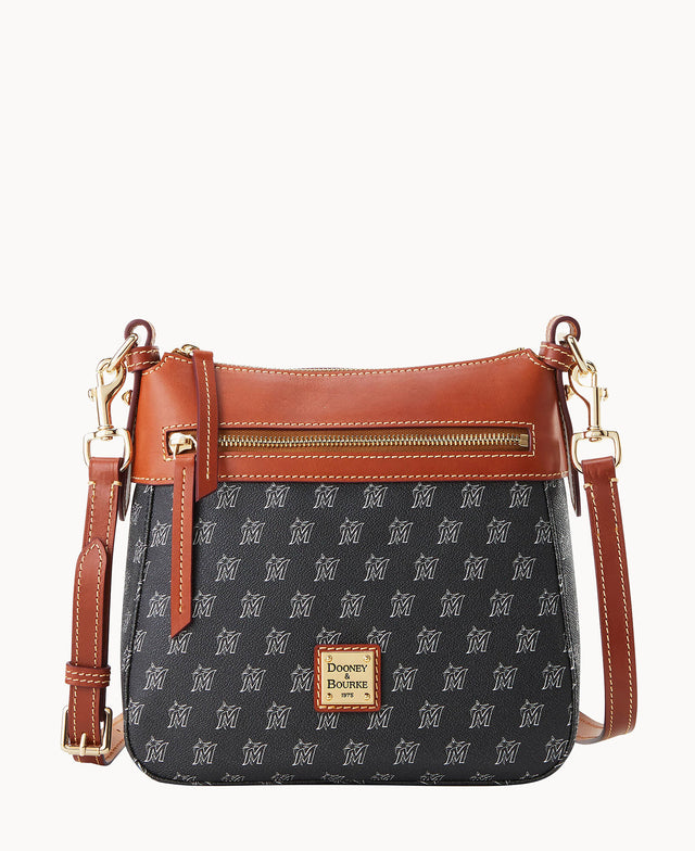 A small crossbody purse with a brown leather trim, gold zipper, and adjustable strap. The main body is black with a repeating white M pattern and a gold Dooney & Bourke logo on the front.