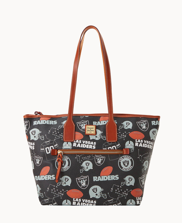 A black tote bag with brown leather handles and trim, featuring a Las Vegas Raiders football team print, including logos, helmets, and the team name. The bag has a front zip pocket and a zipper closure on top.