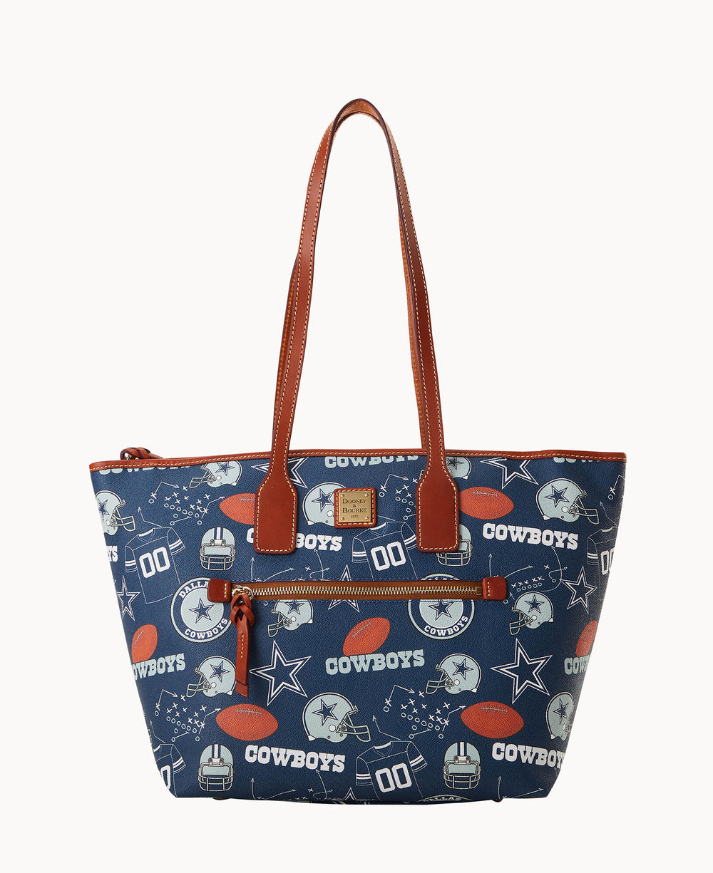 A navy blue tote bag with brown handles and trim, featuring Dallas Cowboys football-themed graphics, including helmets, footballs, stars, and the word Cowboys in white, along with play diagrams.