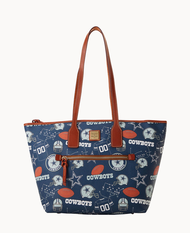 A navy blue tote bag with brown handles and trim, featuring Dallas Cowboys football-themed graphics, including helmets, footballs, stars, and the word Cowboys in white, along with play diagrams.