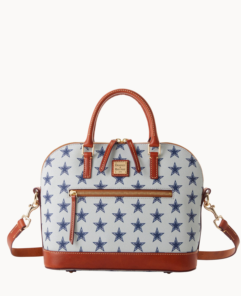 A white handbag with blue stars, brown leather handles, trim, and detachable strap, gold-tone hardware, a front zipper pocket, and a small Dooney & Bourke logo patch.