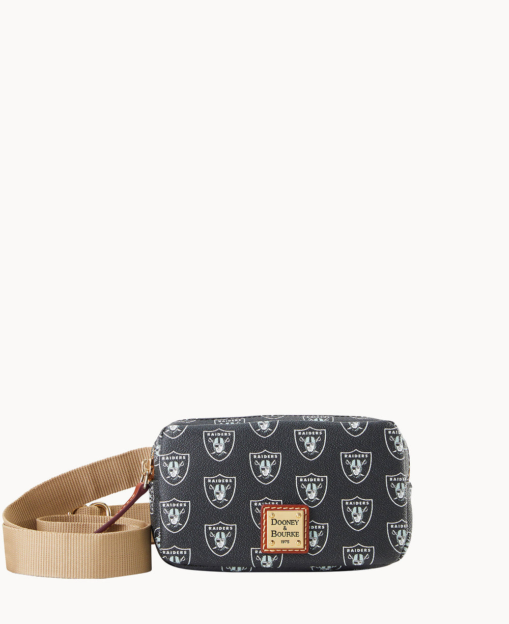 A small black crossbody bag with a tan strap, featuring a repeating Las Vegas Raiders logo pattern and a Dooney & Bourke label on the front.