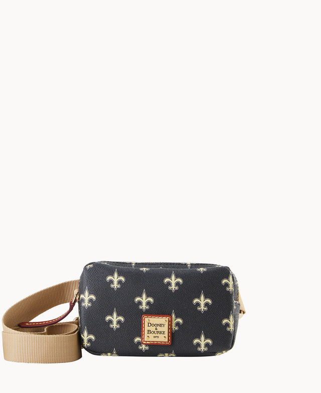 A small black crossbody bag with a tan adjustable strap, decorated with a repeating white fleur-de-lis pattern and a square Dooney & Bourke logo patch on the front.