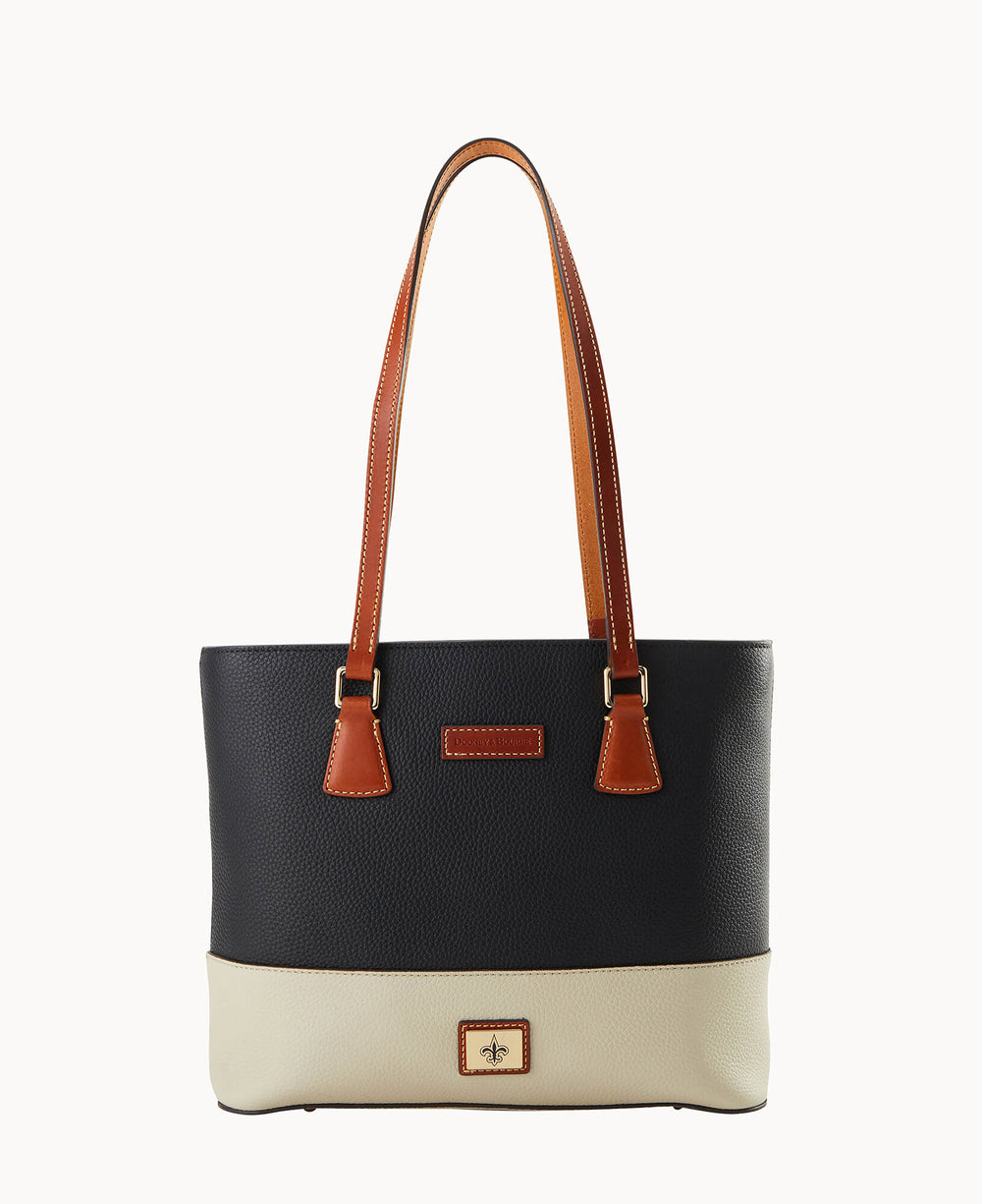 A two-tone tote bag with dark navy upper and cream lower sections, featuring brown leather shoulder straps and gold-tone hardware. The bag has a rectangular shape and a small decorative emblem on the front.