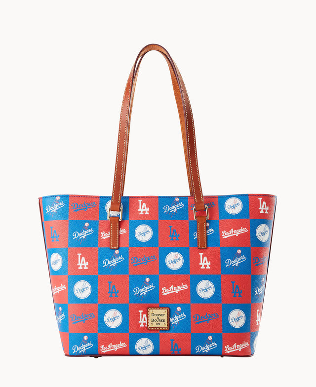 A tote bag with brown handles features a red and blue checkered pattern decorated with white LA Dodgers logos and text. A gold and brown Dooney & Bourke label is attached to the front.