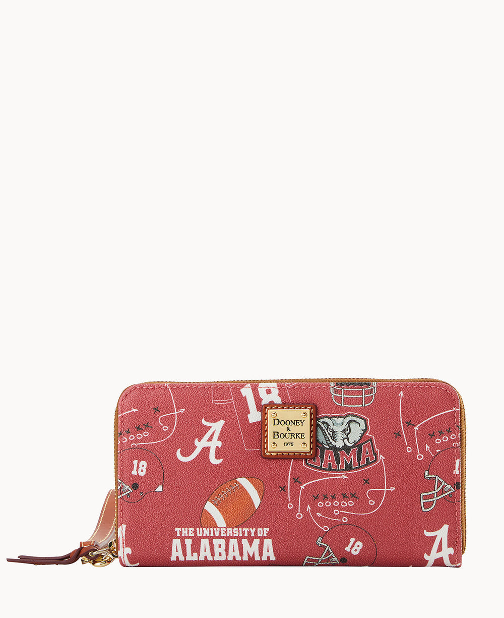 A red zippered wallet with University of Alabama-themed designs, including footballs, helmets, the Alabama A logo, elephant mascot, and The University of Alabama text, with a Dooney & Bourke label on the front.