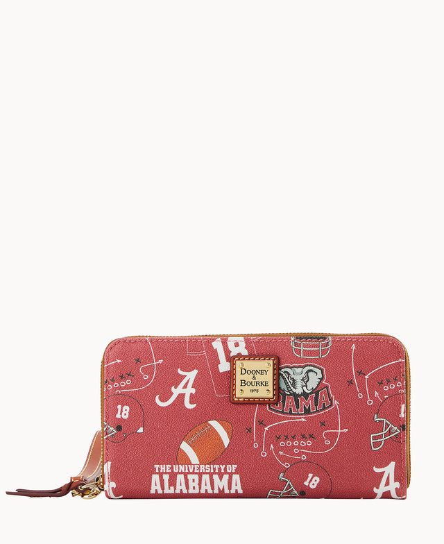 A red zippered wallet with University of Alabama-themed designs, including footballs, helmets, the Alabama A logo, elephant mascot, and The University of Alabama text, with a Dooney & Bourke label on the front.