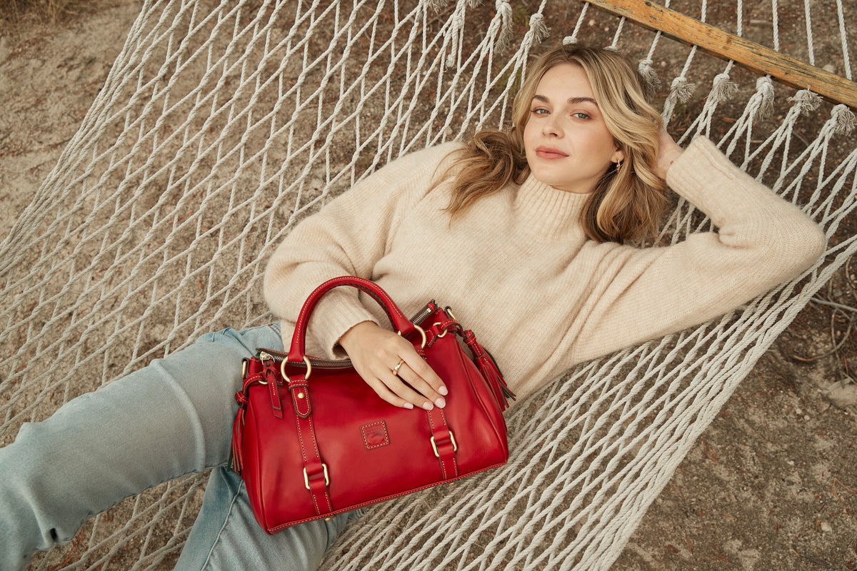 A woman laying on a hammock, carrying a red Dooney & Bourke Florentine Satchel.