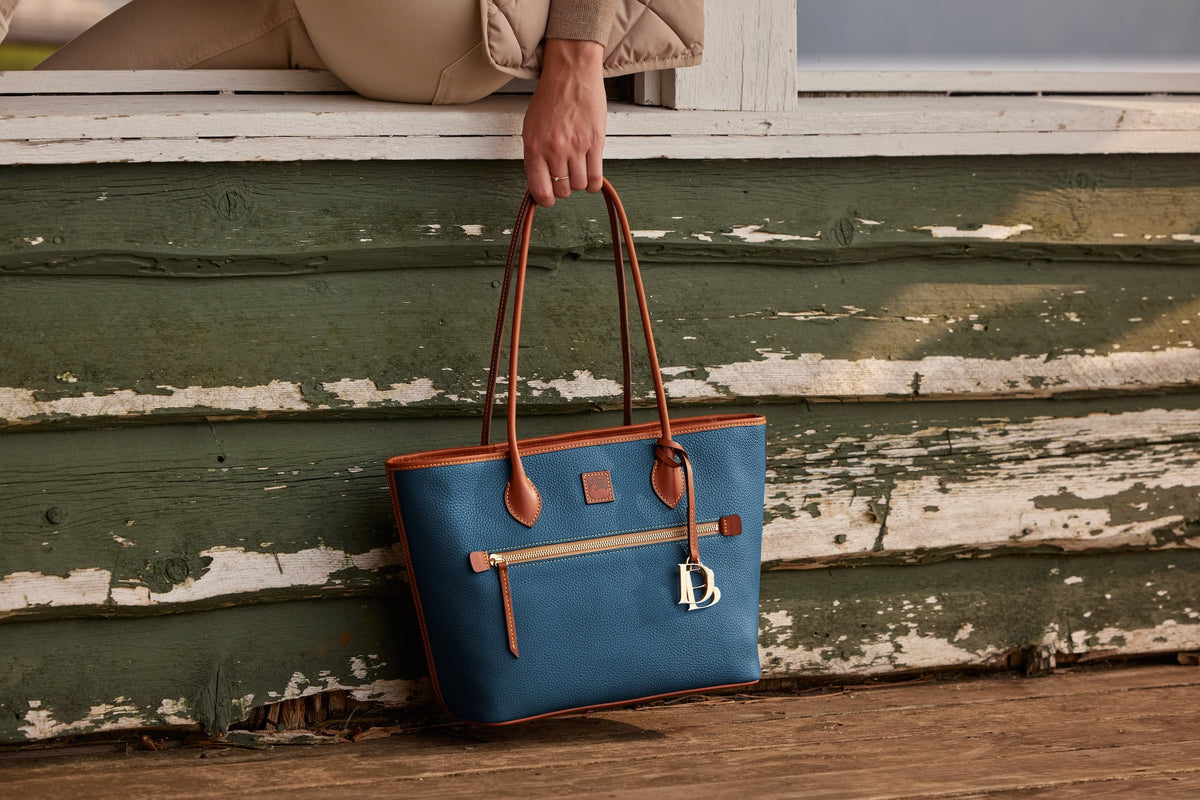 A woman sitting in a chair holding the All Weather Leather Domed Satchel
