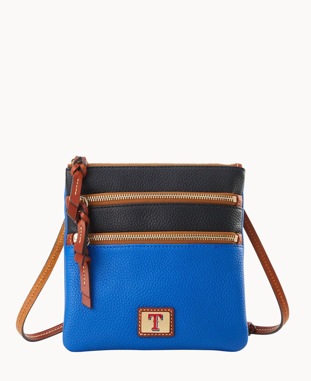 A small crossbody bag with a tan strap, two zippered compartments, a blue lower half, black upper half, and a patch featuring a red letter T on the front.
