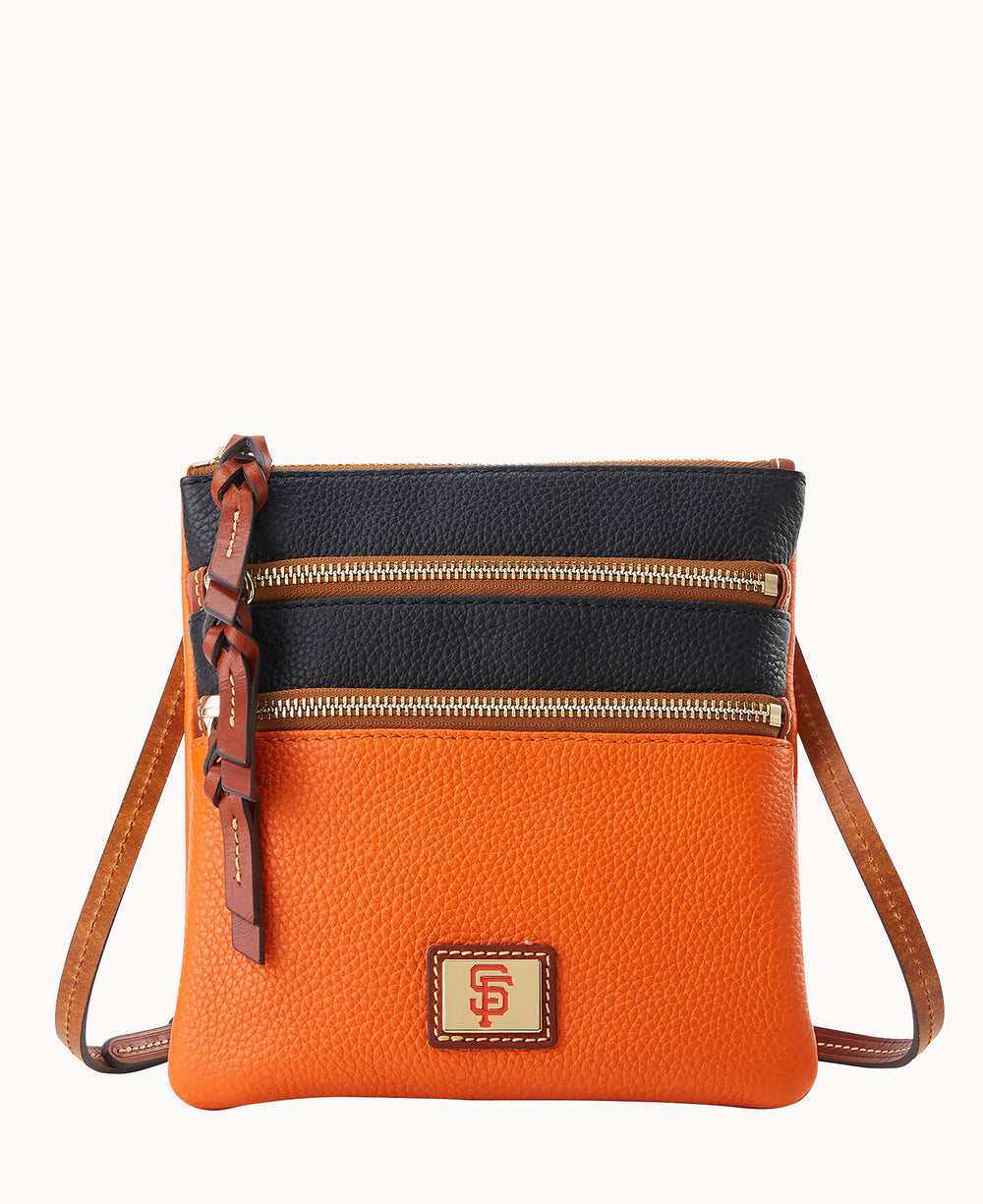 A small crossbody bag with a textured orange base, black top panel, two gold zipper compartments, brown strap, and a square logo patch on the front.