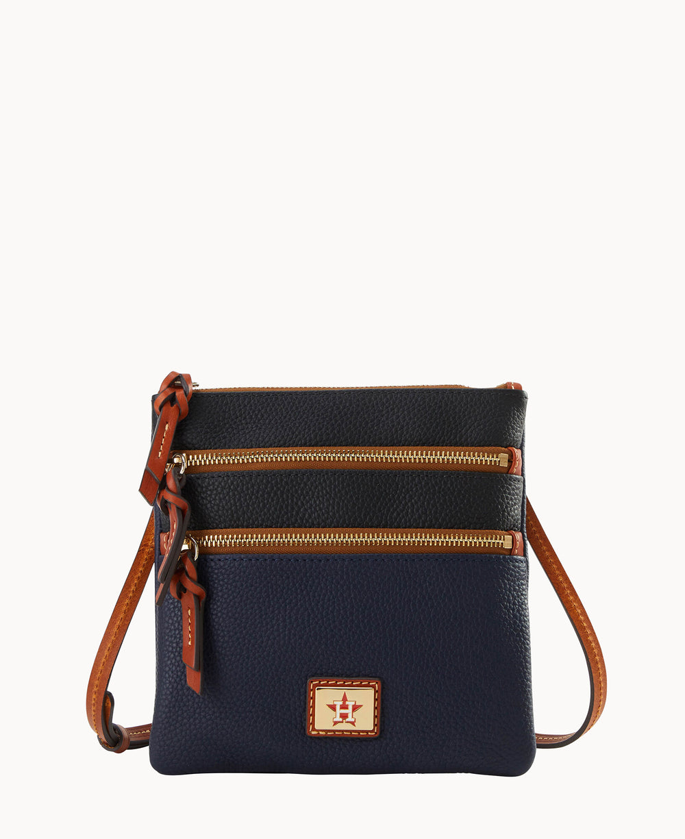 A small, textured leather crossbody bag with two front zippered pockets, brown trim, a tan strap, and a rectangular logo patch on the front. The bag is navy blue and dark brown with gold zippers.