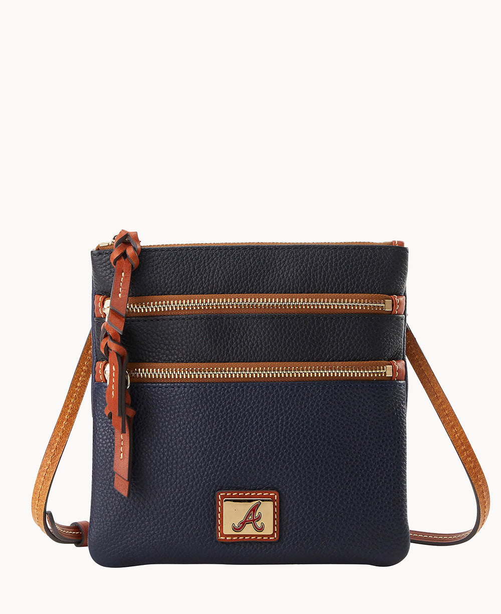 A small navy blue crossbody bag with two front zippered pockets, tan trim, a matching tan strap, and a patch featuring a red letter A on the front.