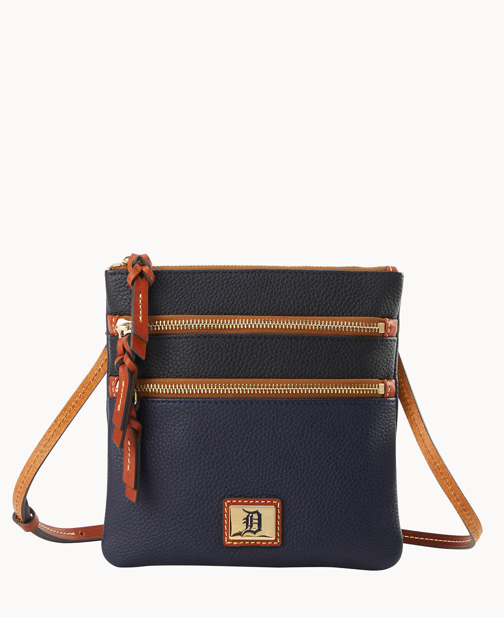 A navy blue leather crossbody bag with tan trim, two front zippered pockets, a tan adjustable strap, and a gold-tone logo plate on the front.