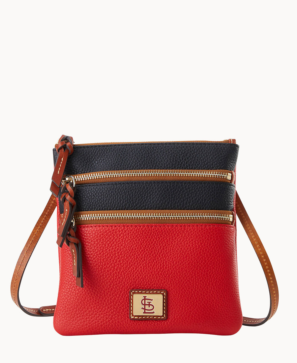 A small crossbody bag with a red bottom half and black top half, brown adjustable strap, two gold zipper pockets, and a stitched logo patch on the front.