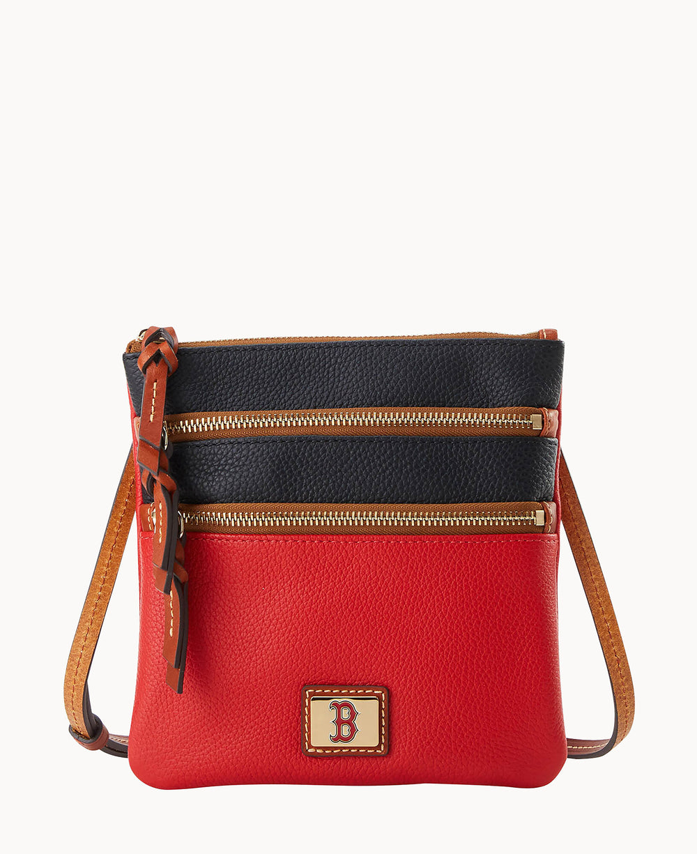 A small crossbody bag with a red bottom half, black top half, two zippered compartments, tan strap, and a patch featuring a red letter B on the front.