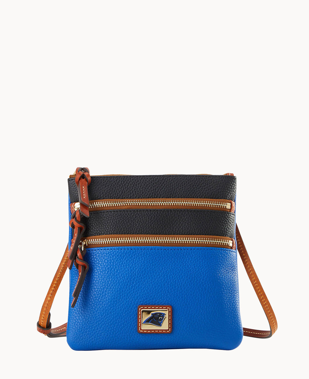 A small crossbody bag with a blue bottom half, black top half, two gold zippers, brown leather trim, and a brown adjustable strap. A small logo patch is on the front.