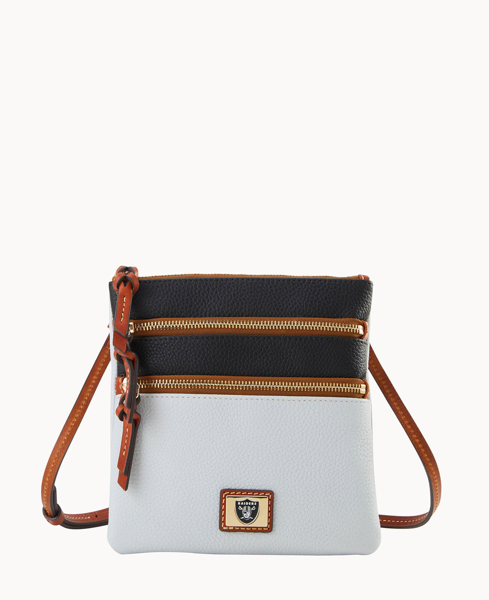 A small crossbody bag with a white lower half, black upper half, two gold zippers, brown leather strap, and a gold logo plate on the front, displayed against a plain white background.