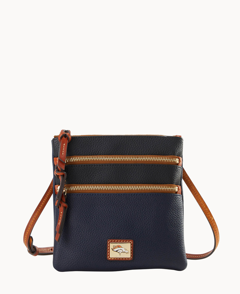 A small navy blue leather crossbody bag with two front zippered pockets, brown leather trim, matching strap, and a rectangular logo patch at the bottom center.