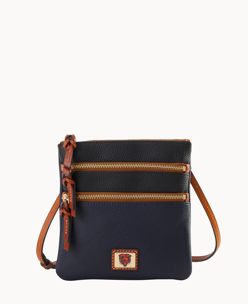 A small navy blue crossbody bag with two front zippered pockets, brown leather accents, and a long adjustable strap. A stitched logo patch is on the front lower section.