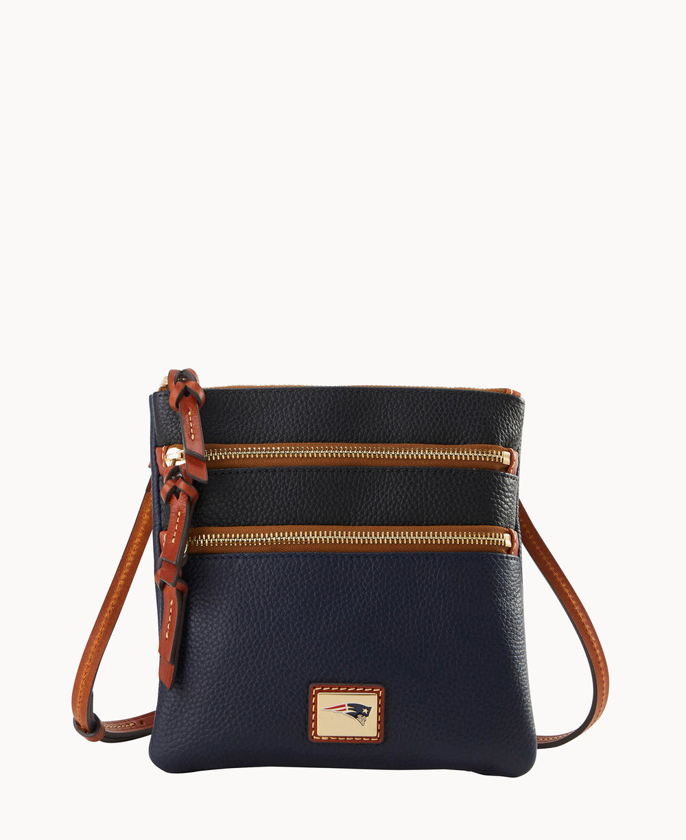 A small, navy blue pebbled leather crossbody bag with two exterior zippered pockets, brown leather trim, an adjustable strap, and a gold-tone logo plate on the front.