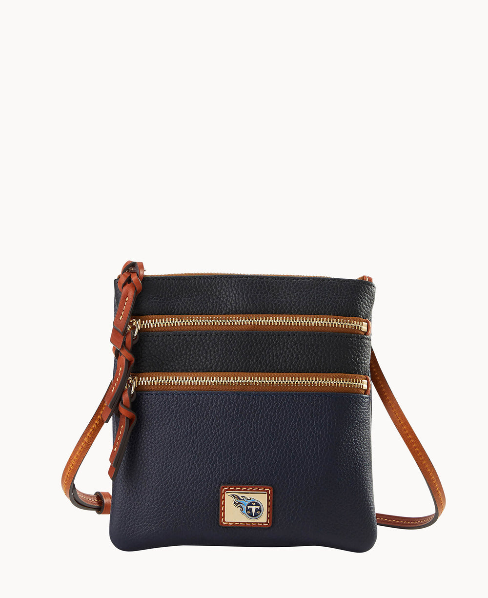 A small, navy blue leather crossbody bag with brown leather trim, two front zippered pockets with gold zippers, and an adjustable brown strap. The front features a rectangular logo patch.