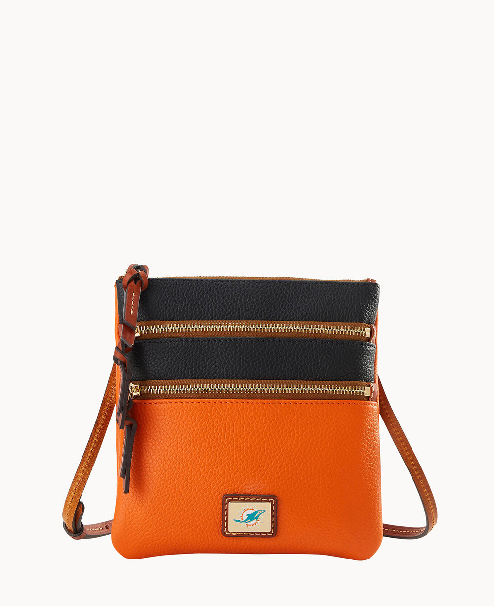 A small crossbody bag with an orange body, black top section, two gold zippers on the front, brown leather strap, and a tan logo patch with a blue and white emblem near the bottom.