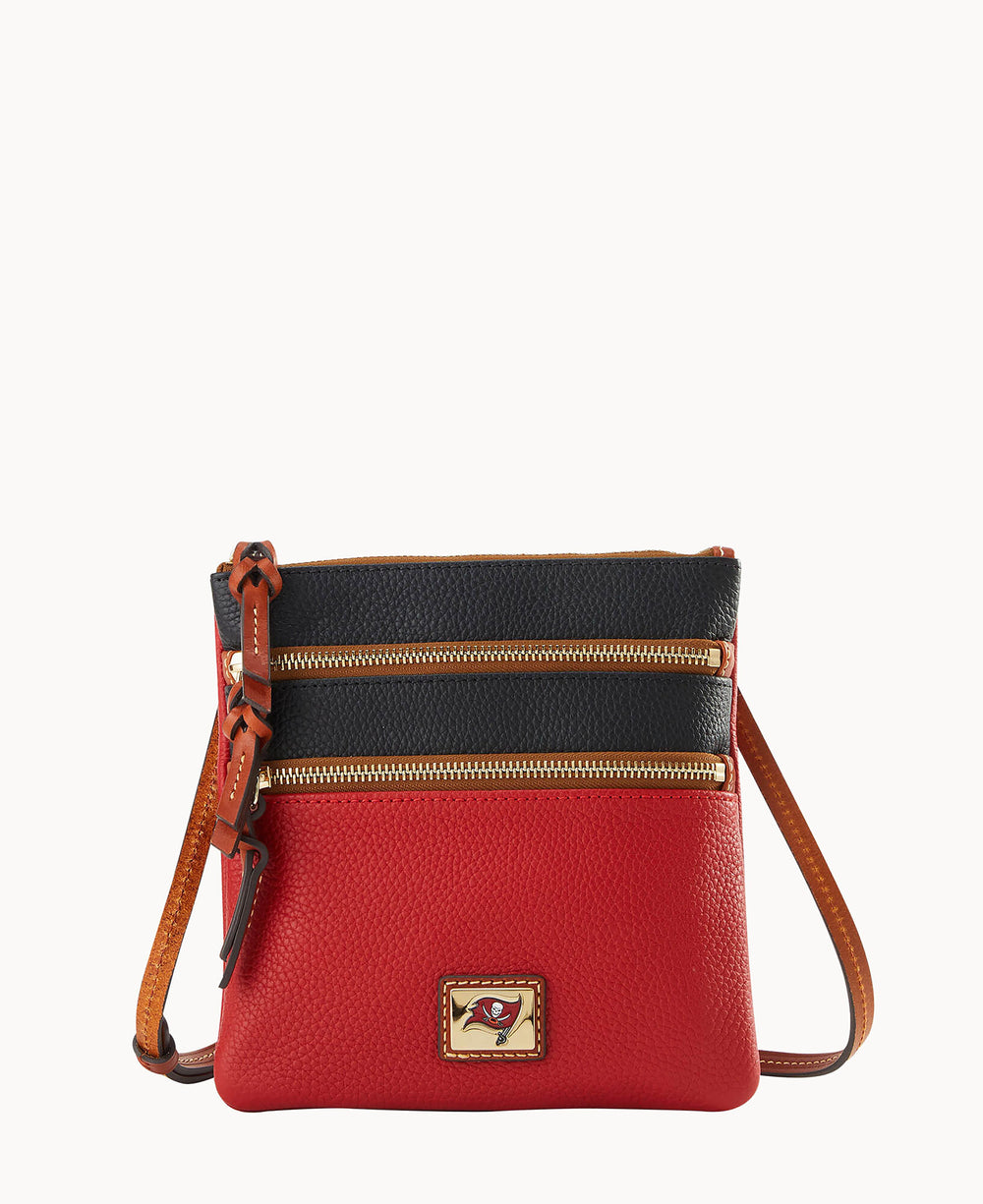A small crossbody bag with a red bottom half, black top half, two gold zippers on the front, brown edges, and a brown adjustable strap. A gold square logo plate is on the front near the base.