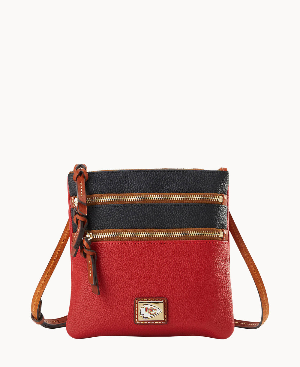 A small crossbody bag with a red lower half, black upper section, tan edges, two front zippered pockets, and an emblem featuring the Kansas City Chiefs logo.