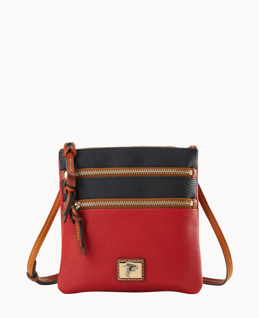 A small crossbody bag with a black top section and red bottom section, featuring two front zippered pockets with gold zippers, tan trim, and a tan shoulder strap. A logo patch is visible on the lower front.