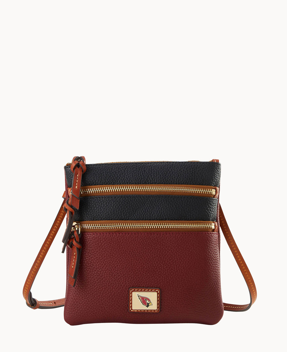 A small crossbody handbag with a pebbled leather texture, featuring a black top section, a burgundy bottom section, tan leather strap, two zippered front pockets, and a small logo patch on the front.