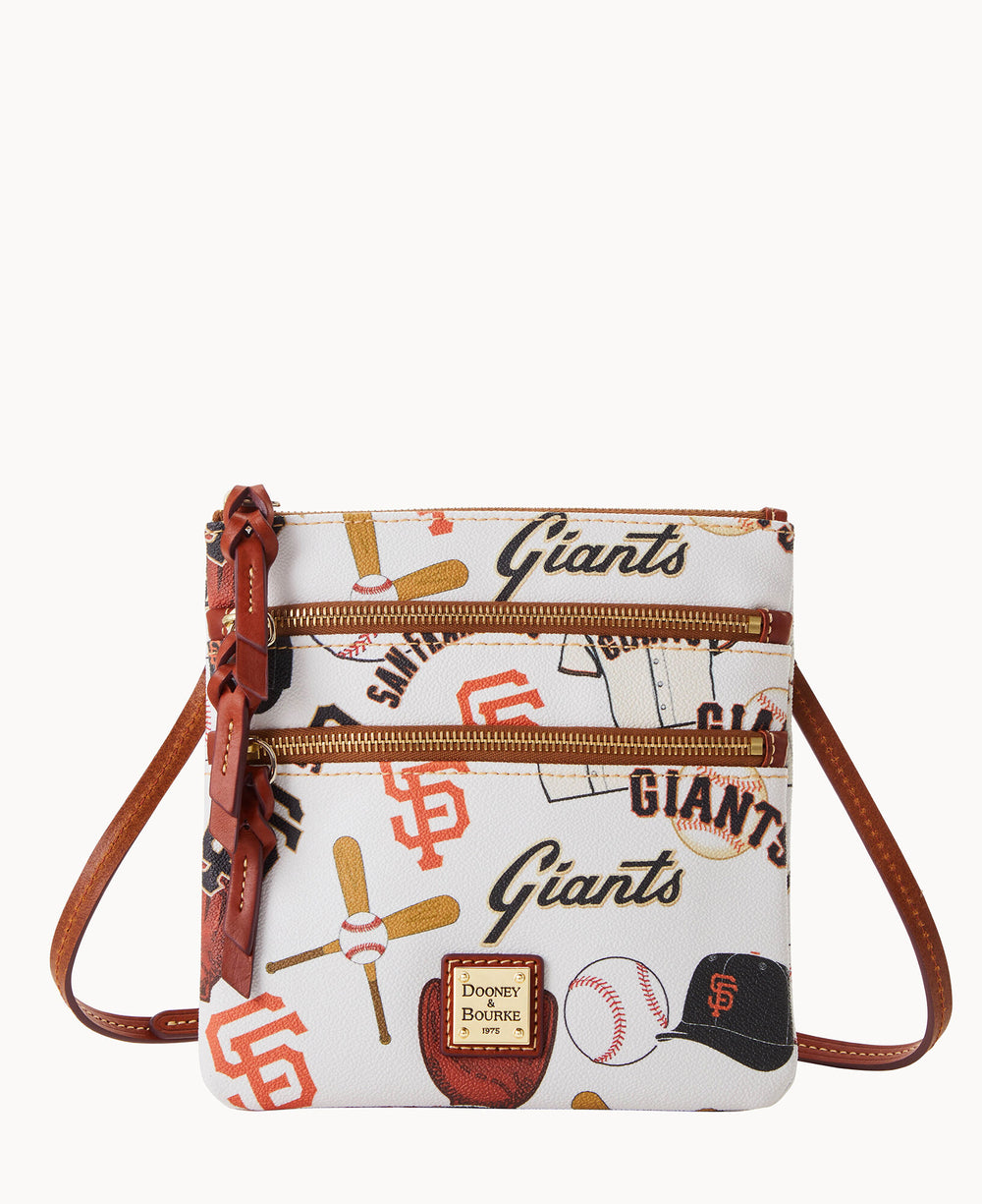 A small crossbody bag with brown leather straps and zippers, featuring a San Francisco Giants-themed print with team logos, baseballs, bats, and caps on a white background.