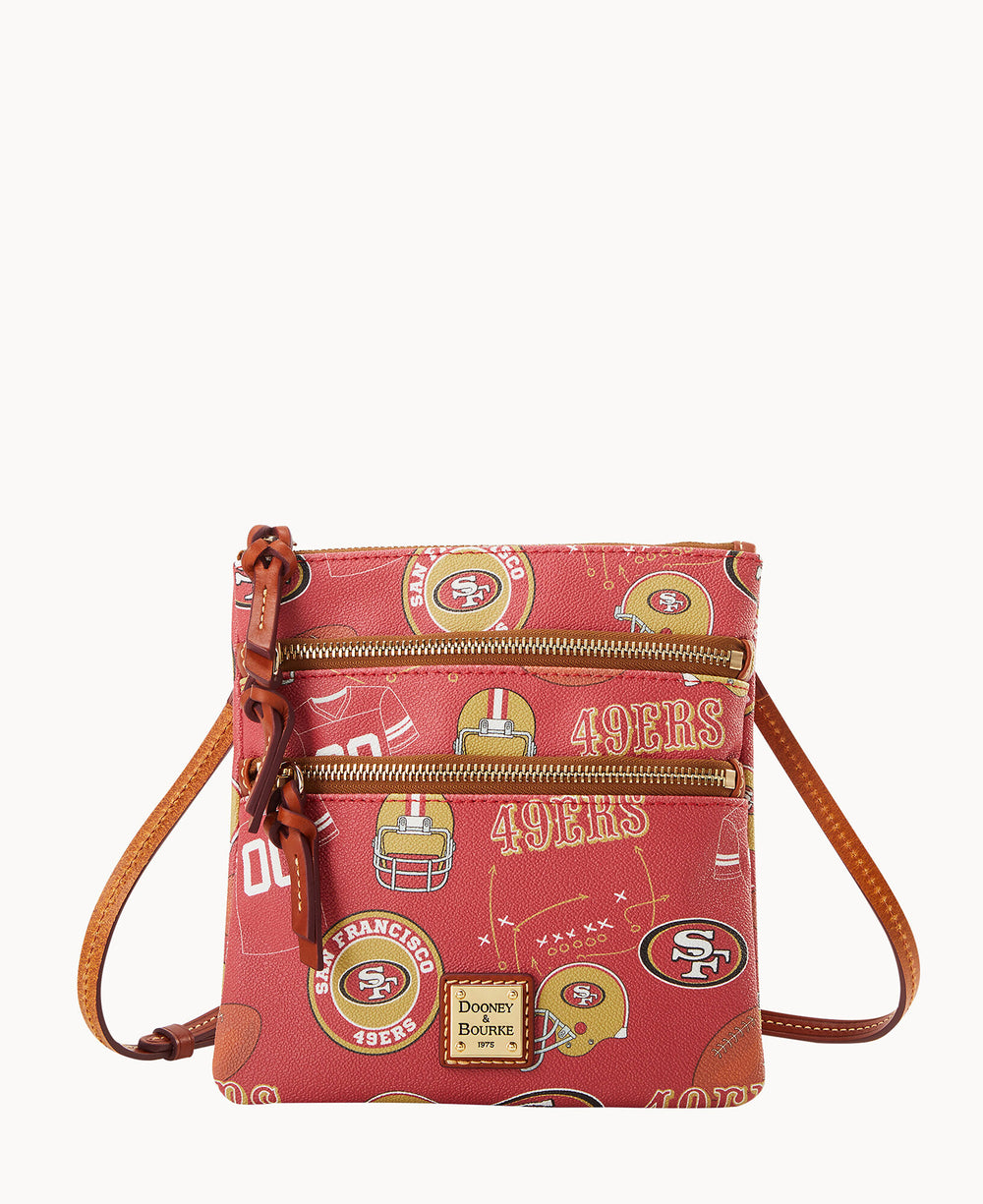 A red crossbody bag with brown straps features San Francisco 49ers logos, football helmets, and 49ERS text, plus two front zippered pockets and a Dooney & Bourke label at the bottom.
