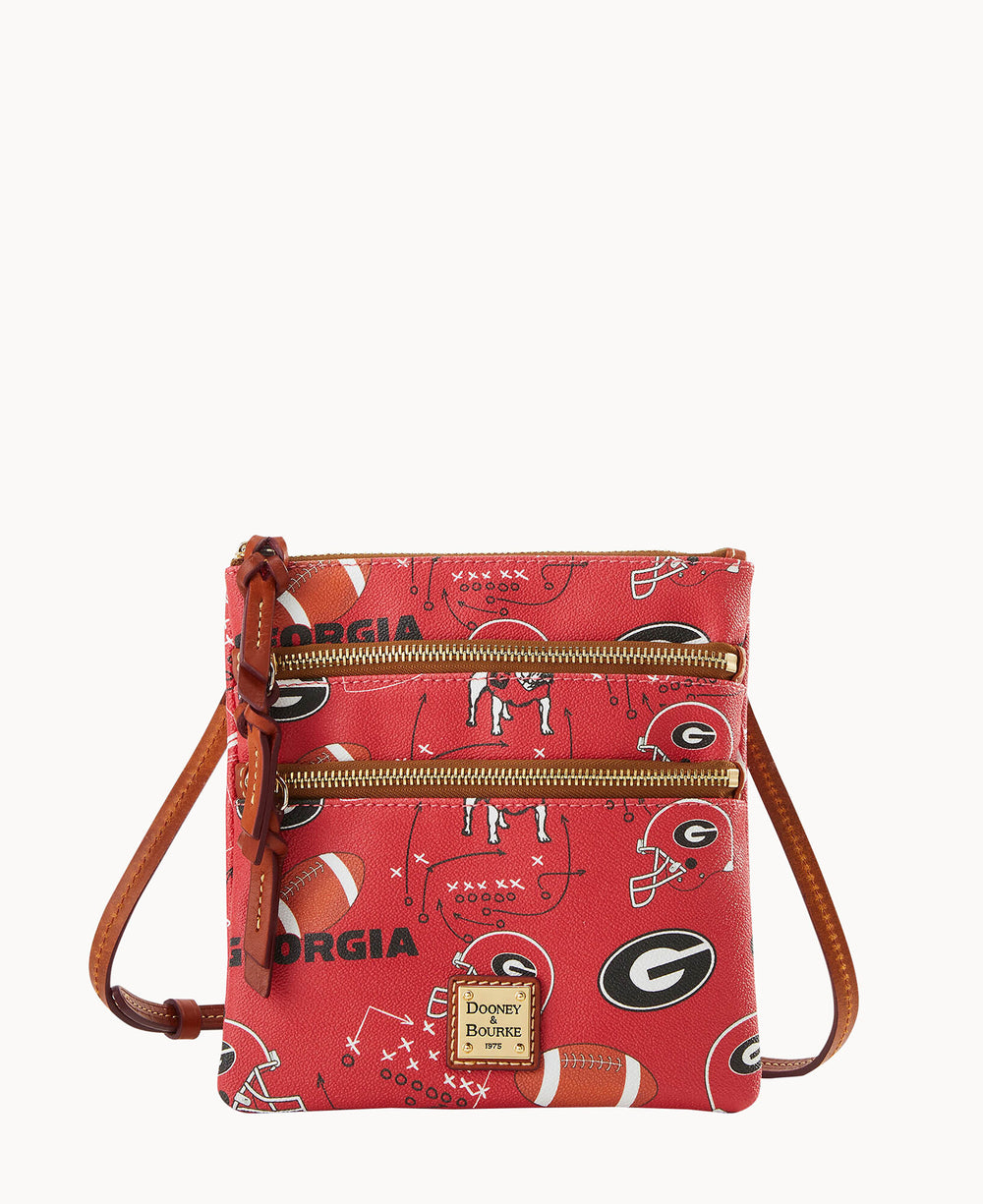 A red crossbody bag with brown leather strap and gold zippers, featuring a football-themed print with â€œGeorgia,â€ footballs, helmets, and play diagrams. The Dooney & Bourke logo is on a small square patch at the bottom.