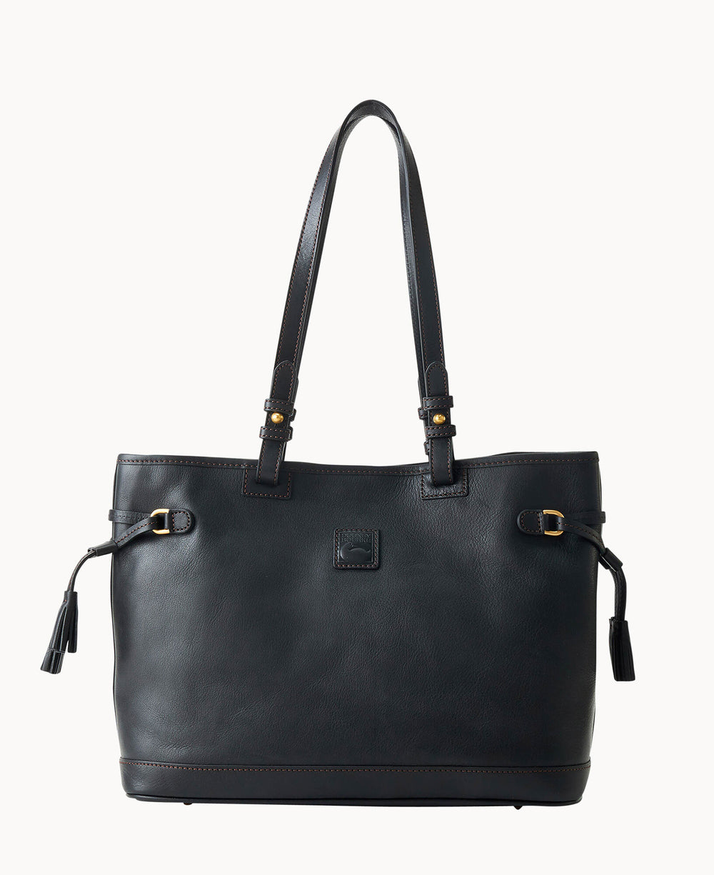 A black leather tote bag with two long handles, gold-tone buckle accents, tassel details on each side, and a small square logo patch on the front. The bag has a simple, elegant design.
