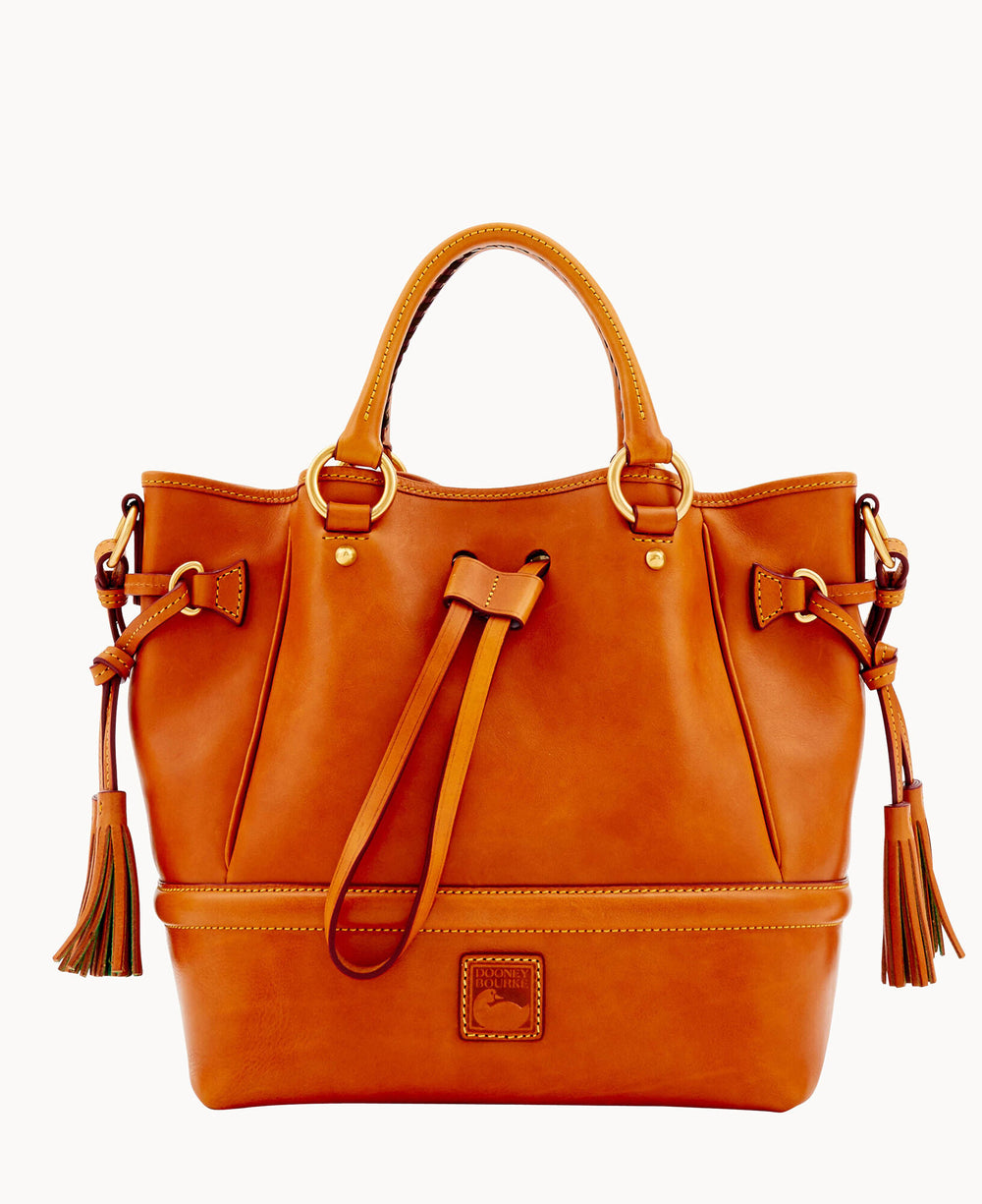 A tan leather handbag with two handles, decorative tassels on each side, gold hardware, and a leather logo patch on the front, against a white background.