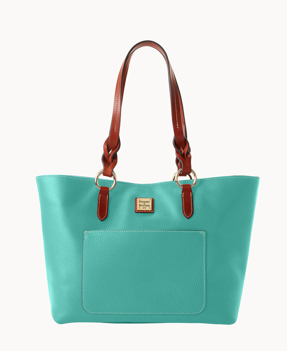 A turquoise leather tote bag with brown braided handles, gold hardware, a front pocket, and a small gold logo plate on the front.