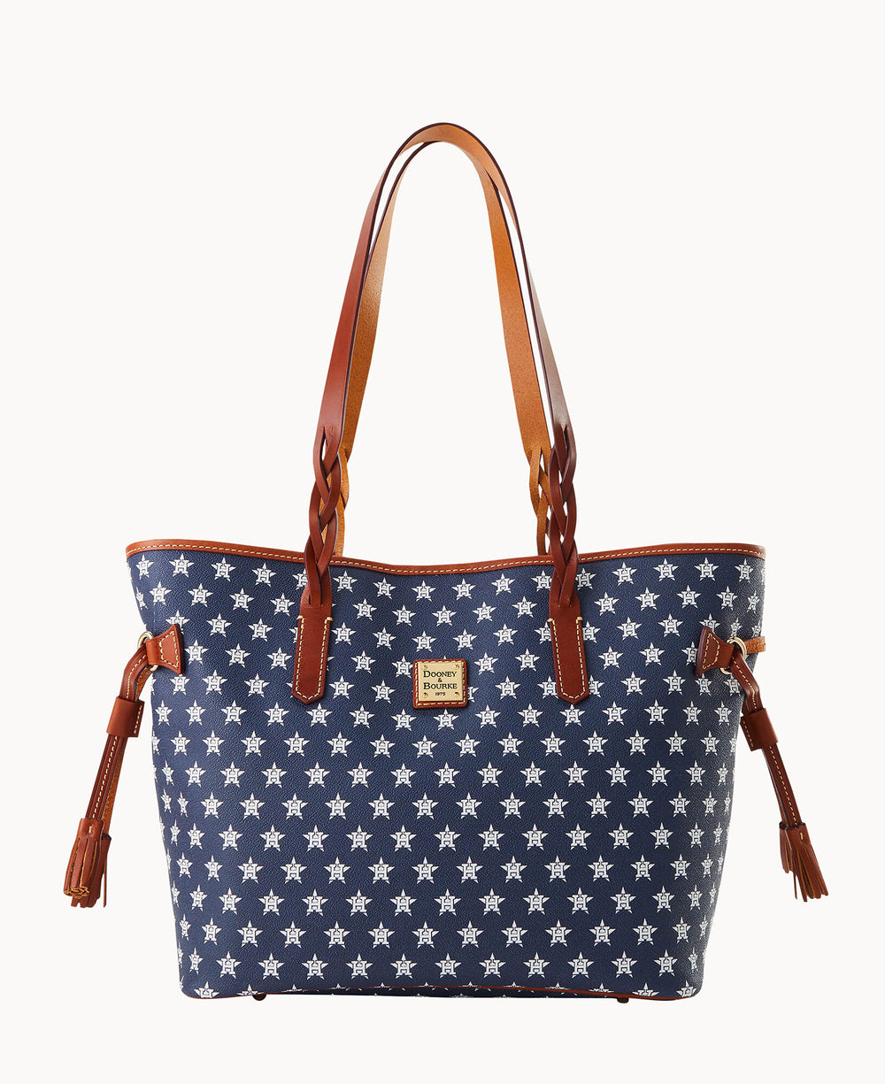 A blue tote bag with white star patterns, brown leather handles, and brown leather tassel accents on each side, displayed on a white background.