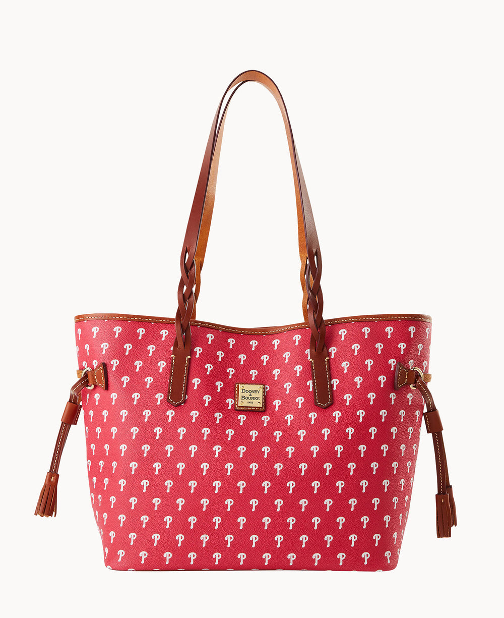 A red tote bag with brown leather handles and trim, decorated with a repeating white P pattern and small tassels on each side.
