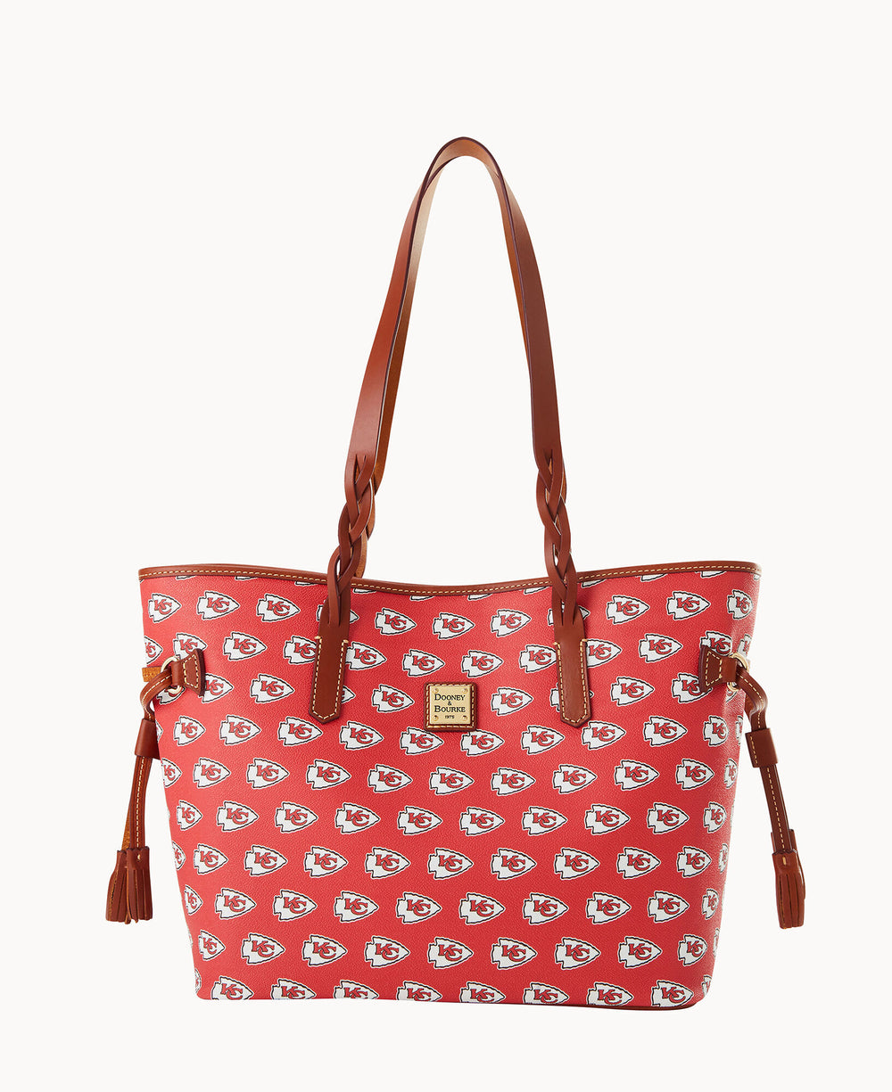A red tote bag with brown handles, decorated with a repeating Kansas City Chiefs logo pattern and a small gold Dooney & Bourke label on the front.