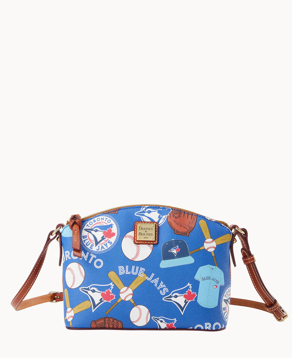 A blue crossbody bag with brown leather straps features Toronto Blue Jays logos, baseballs, gloves, bats, caps, and maple leaves printed in a colorful, playful design.