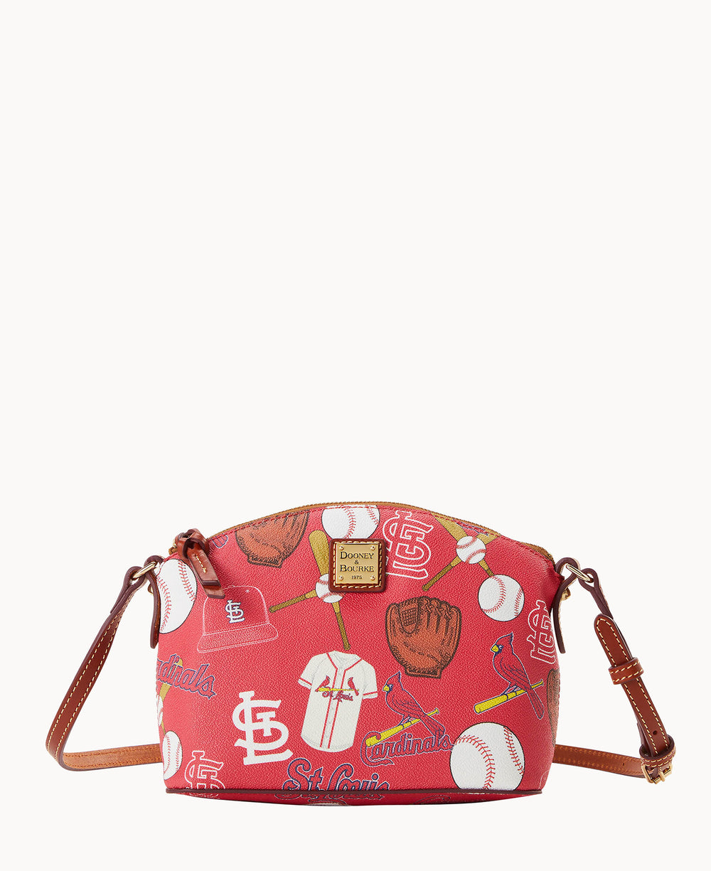 A red crossbody bag with brown straps, featuring aÂ St. Louis Cardinals baseball-themed print, including baseballs, jerseys, gloves, bats, and team logos. The bag has a gold Dooney & Bourke logo plaque on the front.
