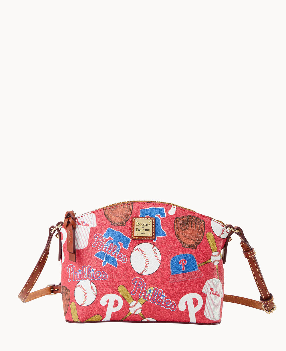 A red Dooney & Bourke crossbody bag featuring Philadelphia Phillies logos, baseballs, gloves, bats, and caps, with brown leather trim and an adjustable strap.