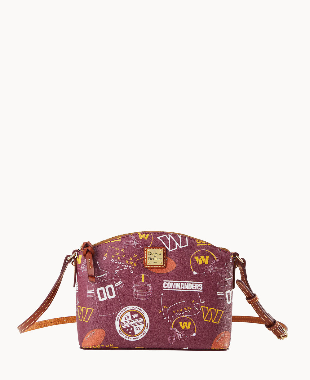 A small maroon crossbody bag with brown leather accents, featuring a Washington Commanders football team print, including helmets, jerseys, logos, and footballs.