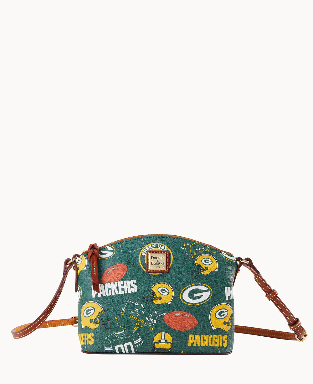 A small crossbody bag with brown leather straps, featuring a green background and Green Bay Packers-themed prints, including footballs, helmets, the Packers logo, and the word PACKERS.