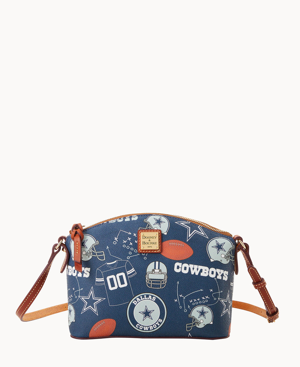 A small blue crossbody bag with brown leather straps featuring Dallas Cowboys logos, football helmets, footballs, stars, and the word COWBOYS printed in white across the front.