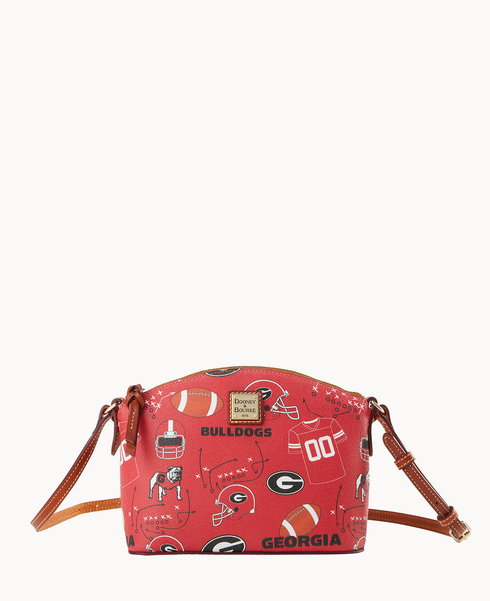 A red crossbody bag with brown leather straps features Georgia Bulldogs logos, footballs, helmets, and mascot illustrations, and a gold Dooney & Bourke label on the front.